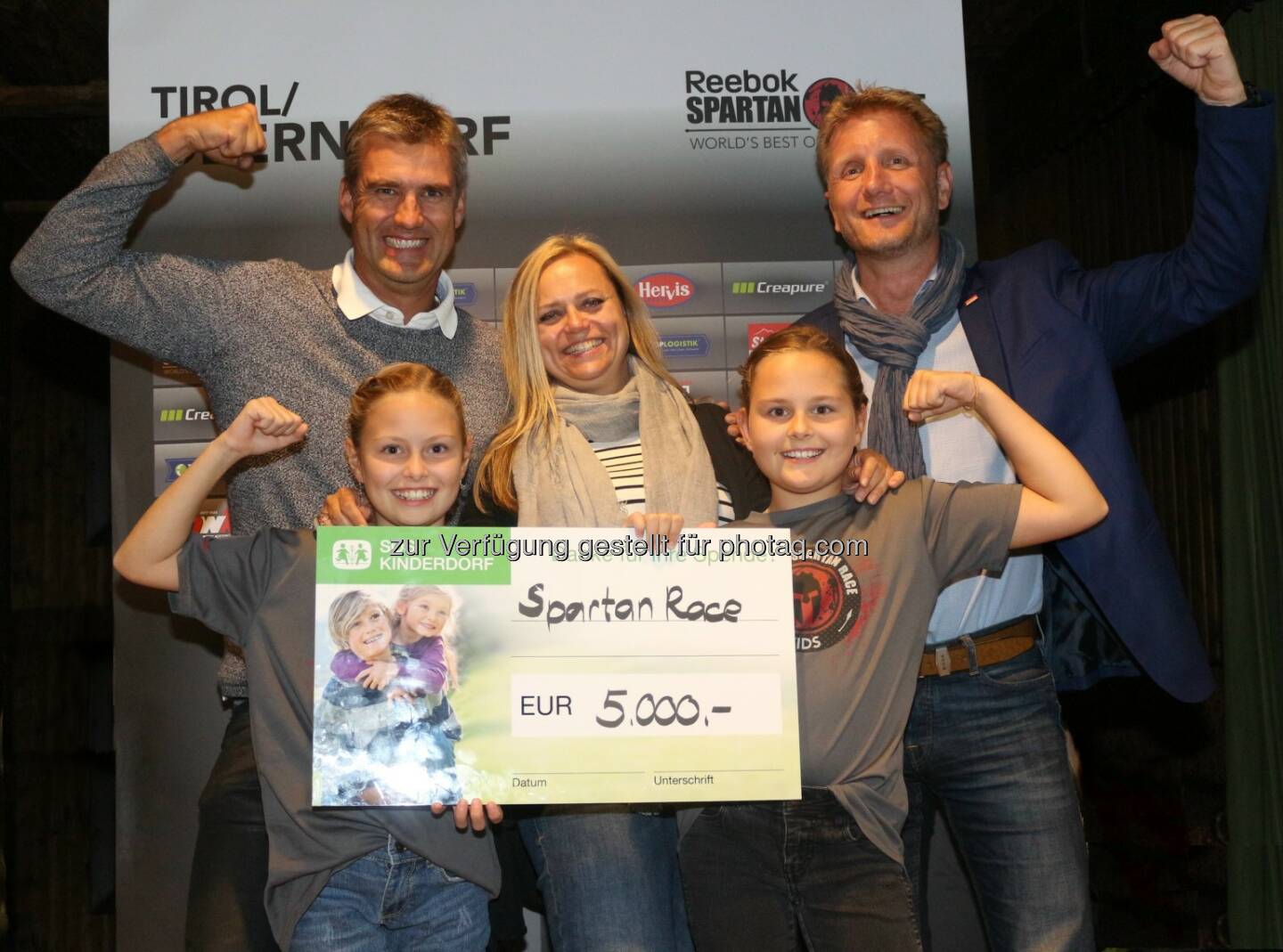 Gemeinsame Freude über erfolgreiche Aktion: Sparten Race Organisator Helge Lorenz (im Bild links) und Gernot Riedl vom Tourismusverband St. Johann in Tirol (rechts) übergeben Manuela Mader von SOS-Kinderdorf einen 5.000 Euro Scheck. - Kitzbüheler Alpen - St. Johann Oberndorf-Kirchdorf-Erpfendorf: Spartan Race Oberndorf in Tirol spendet 5.000 Euro an SOS Kinderdorf (Fotocredit: Spartan Race)