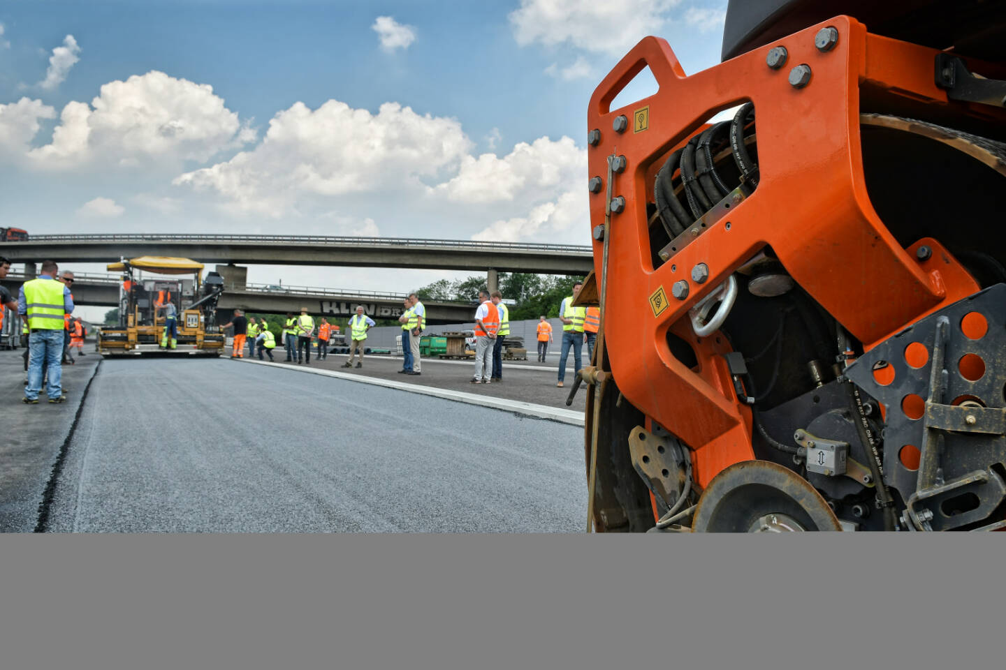 NaHiTAs (Nachhaltiger High-Tech Asphalt) - Das mit Titandioxid versetzte Granulat wird über den fertigerintegrierten Streuer (hinten im Bild) in die Asphaltdeckschicht eingebunden.
Bildnachweis: STRABAG AG